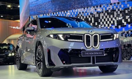 New BMW iX3 electric SUV in gray on display at auto show with illuminated kidney grille and blue light backdrop