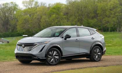 Gray Nissan Ariya parked on a gravel path beside green fields and trees.