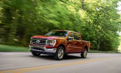 Red Ford F-150 pickup driving along a tree-lined road with motion blur in the surrounding forest.