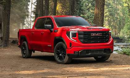 Red GMC Sierra 1500 pickup truck parked in a forest clearing surrounded by tall trees.