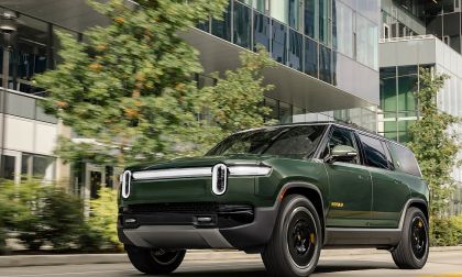 Green Rivian R1S SUV driving past modern buildings in city