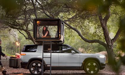 A Rivian R2 all-electric SUV is shown in a tranquil camping scene