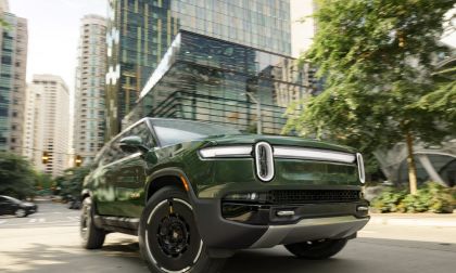 Rivian R1S electric SUV driving through a modern city street with glass skyscrapers and urban traffic.