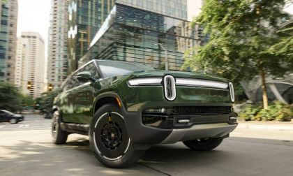 Green Rivian R1S electric SUV driving in a downtown city street with modern buildings