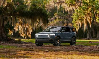 Gray-blue Rivian R1S SUV parked under oak trees draped in Spanish moss, front three-quarter view