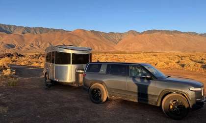 Rivian R1S towing an Airstream trailer at a desert campsite with mountains in the background.