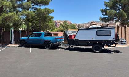Blue Rivian R1T towing an off-road camper trailer while parked beside EV charging stations.