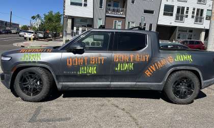 Gray Rivian R1T parked on a city street with “don’t buy junk” graffiti painted on the side.
