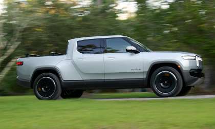 Silver Rivian R1T electric pickup driving past blurred greenery in a side profile view.