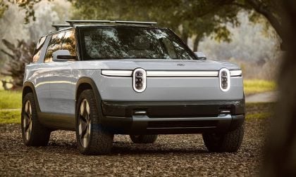 Rivian R1S electric SUV front view parked in a forest setting with soft sunlight