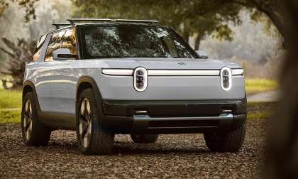Silver Rivian R2S parked on a wooded trail in a front three-quarter view.