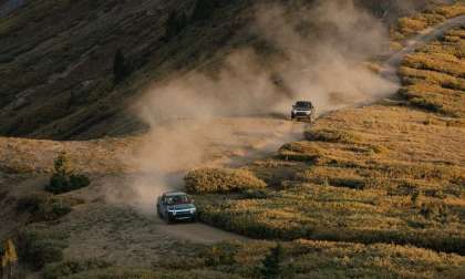 A pair of Rivian R1T pickup trucks are pictured driving on a mountainside trail.