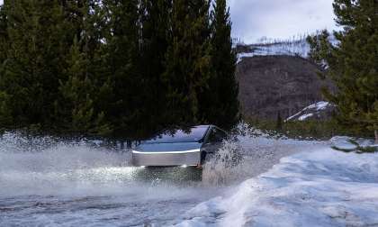 Tesla Cybertruck driving through a snowy water crossing and throwing up a large splash in a winter forest.