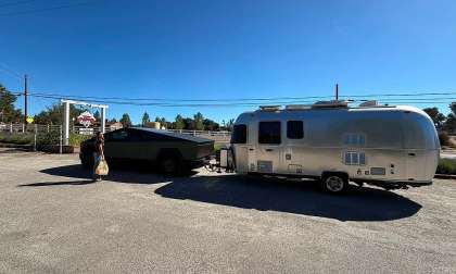 Tesla Cybertruck towing an Airstream travel trailer in a parking lot with a person standing beside the truck.