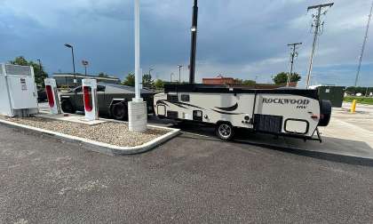 Tesla Cybertruck towing a Rockwood travel trailer while parked at a Tesla Supercharger station
