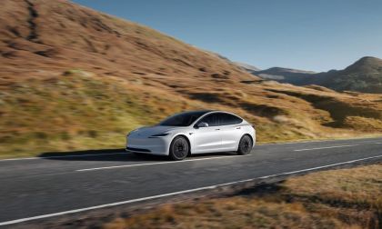 White Tesla Model 3 driving on a scenic highway through rolling hills, emphasizing electric range and minimalist design.