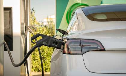 White Tesla plugged into an EV charger, shown close up from the rear quarter.