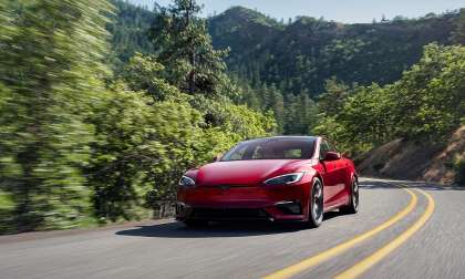 Red Tesla Model S driving on a winding road through a forested mountain landscape.