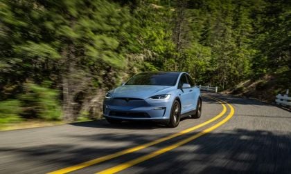 Tesla Model X blue electric vehicle driving on winding forest highway