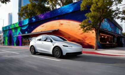 A white Tesla Model Y driving past a colorful city mural.