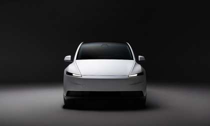 Front view of a white Tesla Model Y in a dark studio with slim LED headlights illuminated.