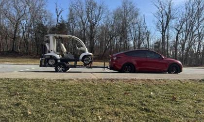 Red Tesla Model Y towing a trailer with a golf cart, electric SUV hauling in parking lot