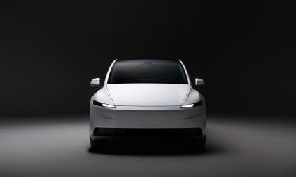 White Tesla Model Y front view in a dark studio setting, highlighting minimalist design and LED headlights