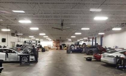 Tesla service center with multiple electric vehicles under repair in spacious, well-lit automotive workshop