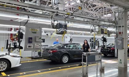 A Toyota factory line worker waves hello while building an American-made Camry on an assembly line