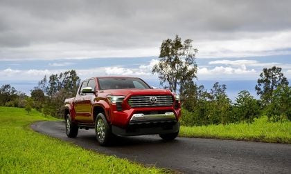 Red Toyota Tacoma driving on scenic road with green hills and ocean background