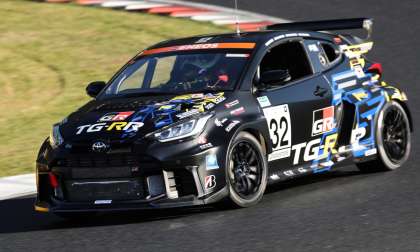 Black Toyota GR Yaris race car with TG-RR racing livery cornering on a racetrack, front three-quarter view