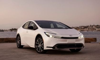 White Toyota Prius hybrid sedan parked near the water at golden hour, angled front view highlighting sleek exterior lines.
