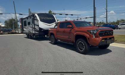 Toyota Tacoma towing an Outback travel trailer in a front three-quarter view near an intersection.