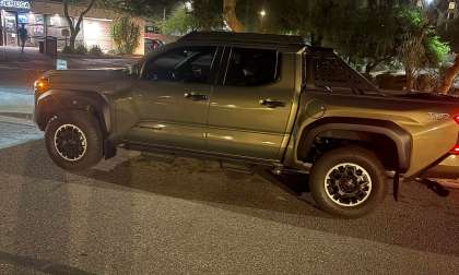 Bronze Oxide Toyota Tacoma Trailhunter parked at night on a city street in side profile.