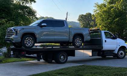 Gray Toyota Tundra loaded on a flatbed tow truck in a residential neighborhood.