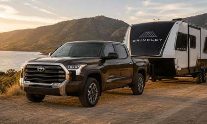 Dark brown Toyota Tundra towing a black and white Brinkley travel trailer beside a lake at sunset