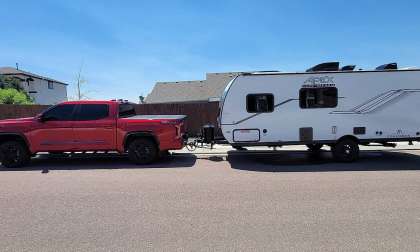 Red Toyota Tundra towing a Coachmen Apex camper trailer in a full side view on a residential street.