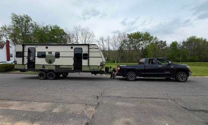 Black Toyota Tundra towing a Forest River NOBO travel trailer on a residential street while a person checks the hitch area.
