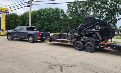 Gray Toyota Tundra towing a large equipment trailer with a black skid steer loaded on it.