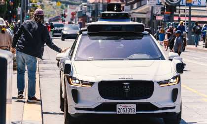 Waymo Jaguar I-Pace robotaxi stopped on a busy city street as a pedestrian passes beside it.