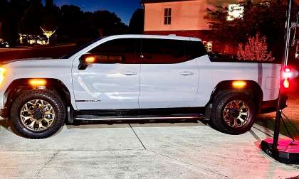 White GMC Sierra Denali parked at night in a driveway beside a basketball hoop with marker lights on.