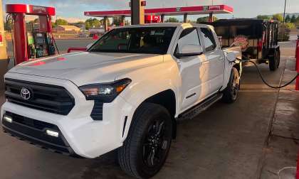 White Toyota Tacoma refueling at a Maverik gas station while towing a black utility trailer.