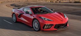 Red Chevrolet Corvette C8 coupe driving at speed on an open desert highway, featuring sharp LED headlights, low-slung stance, and high-performance mid-engine proportions.