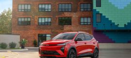 2027 Chevrolet Bolt EV red compact electric SUV front three-quarter view parked in urban setting
