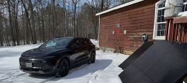 Chevrolet Equinox EV parked outside house connected to portable solar panels in snow