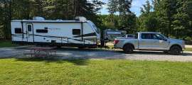 Ford F-150 pickup towing an Astoria travel trailer at a green campground site.