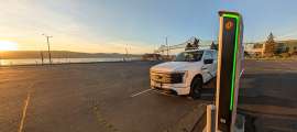White Ford F-150 Lightning charging at a Rivian station near the waterfront at sunset.