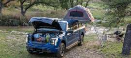 Blue Ford F-150 Lightning XLT set up at a campsite with an open frunk and rooftop tent.