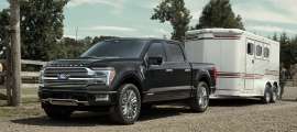 Black Ford F-150 Platinum towing a horse trailer at a ranch, with a person leading a horse alongside a wooden fence
