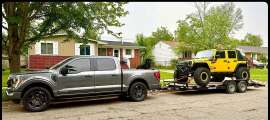 Ford F-150 pickup shown towing a yellow Jeep Wrangler on a flatbed trailer